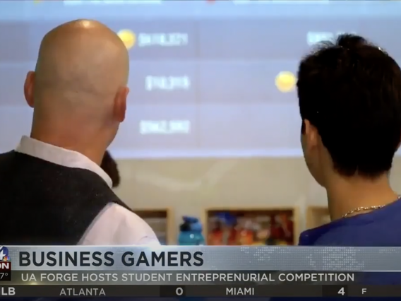 News coverage of two people looking at a leaderboard. Headline: Business gamers, UA FORGE hosts student entrepreneurial competition