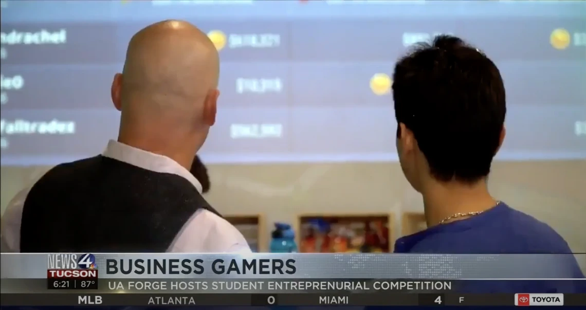 News coverage of two people looking at a leaderboard. Headline: Business gamers, UA FORGE hosts student entrepreneurial competition